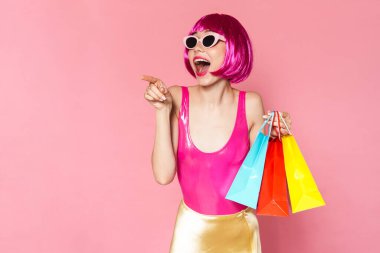 Pembe arka planda izole edilmiş alışveriş çantalarını tutan renkli parlak kıyafetler giyen heyecanlı genç bir kadının portresi.