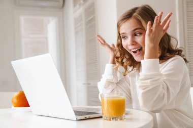 Neşeli bir kızın laptoptan telefon alıp beyaz mutfakta meyve suyu içerken el ele tutuşması.