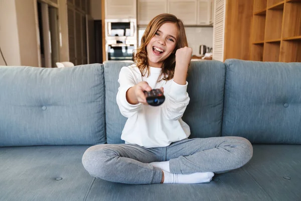 Fénykép Delighted Girl Using Remote Control Making Winner Gesture While — Stock Fotó