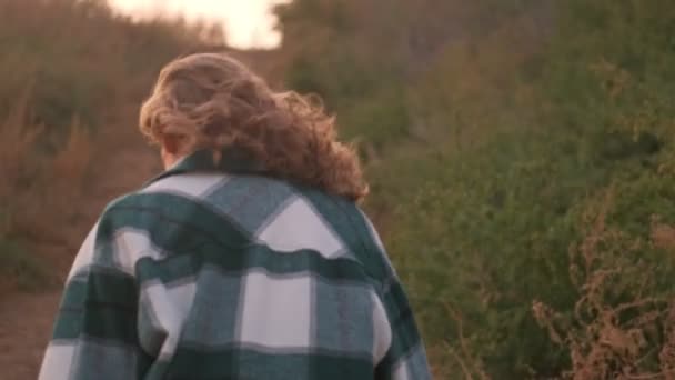 バックビューのブロンド女性を身に着けている再生シャツ歩いて海の近く屋外 — ストック動画