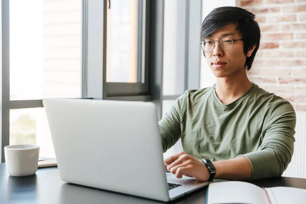 Imagem Bonito Jovem Asiático Homem Vestindo Óculos Usando Laptop Enquanto — Fotografia de Stock