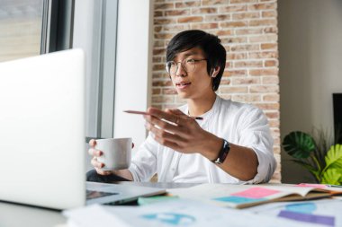 Ofiste otururken kulaklık takan yakışıklı Asyalı bir adamın görüntüsü.