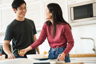 Çekici, neşeli Asyalı çiftin modern mutfakta yemek pişirirken gülüp konuştuğu fotoğraf.