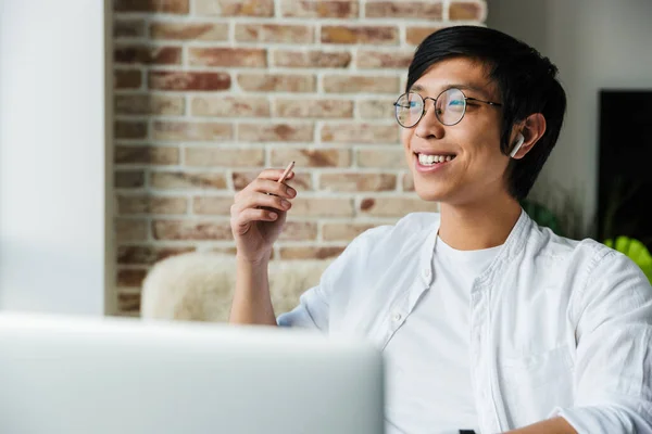 Obraz Przystojnego Młodego Azjatyckiego Mężczyzny Noszącego Słuchawki Pomocą Laptopa Siedzącego — Zdjęcie stockowe