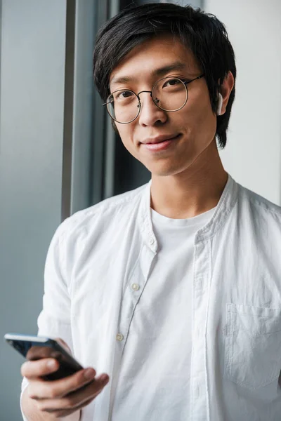 Obraz Przystojnego Młodego Azjatyckiego Mężczyzny Noszącego Słuchawki Pomocą Telefonu Komórkowego — Zdjęcie stockowe
