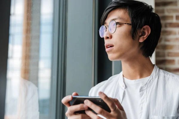 Bild Stilig Ung Asiatisk Man Med Glasögon Som Håller Mobiltelefon — Stockfoto