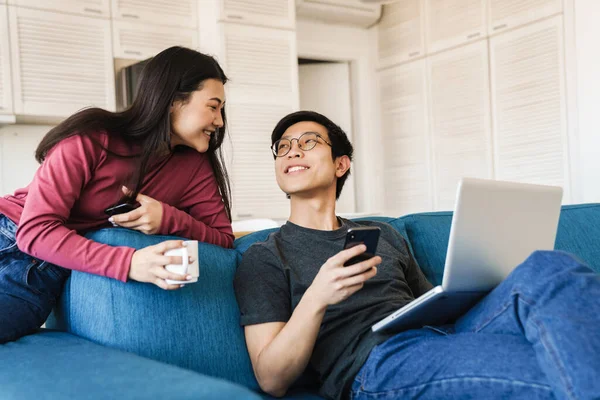 Zdjęcie Uśmiechniętej Pary Azjatyckiej Korzystającej Smartfona Laptopa Podczas Picia Kawy — Zdjęcie stockowe