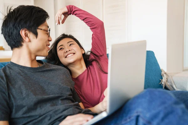 집에서 소파에 노트북을 사용하는 아름답고 즐거운 이시아 부부의 — 스톡 사진