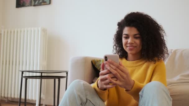Mulher Atraente Africano Alegre Usando Smartphone Enquanto Sentado Chão Sala — Vídeo de Stock