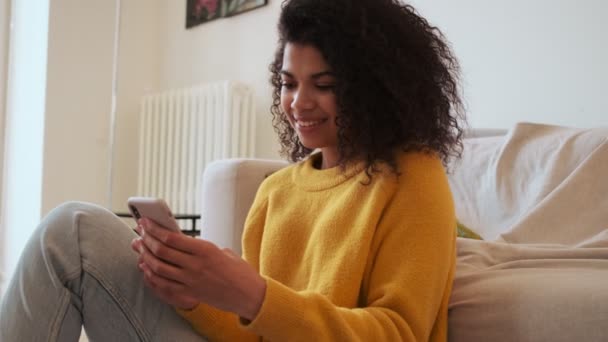 Satisfeito Africano Mulher Atraente Usando Smartphone Enquanto Sentado Chão Sala — Vídeo de Stock