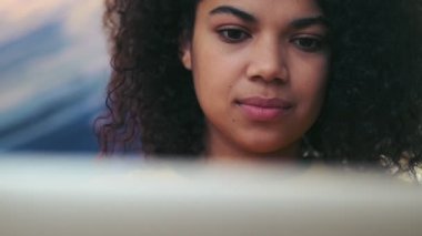 Gülümseyen Afrikalı çekici kadının içeride otururken dizüstü bilgisayar kullanmasını yakından izle.