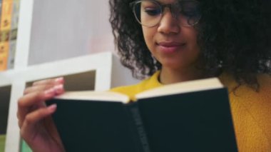 Kapalı alanda otururken gözlüklü çekici bir kadının kitap okumasını yakından izle.