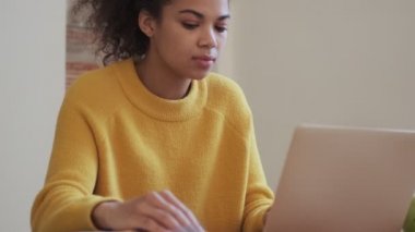 Sakin Afrikalı çekici bir kadın laptopunu içeride masada otururken kullanıyor.