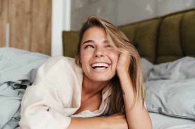 Kafkasyalı neşeli bir kadının evde yatarken kameraya gülüp göz kırparken görüntüsü.