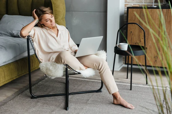 Odaklanmış Sarışın Şık Pijamalı Dizüstü Bilgisayarlı Oturma Odasında Koltukta Oturan — Stok fotoğraf