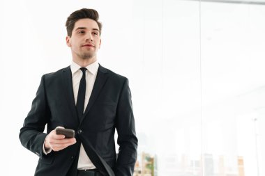 Ofiste cep telefonu kullanarak siyah takım elbise giyen ciddi genç iş adamının görüntüsü