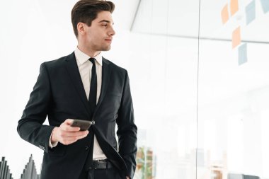 Ofiste cep telefonu kullanarak siyah takım elbise giyen ciddi genç iş adamının görüntüsü