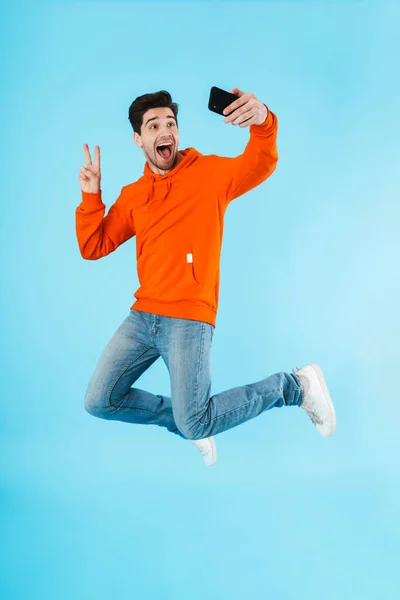 Portrait Cheerful Young Man Wearing Hoodie Jumping Isolated Blue Background — Stock Photo, Image