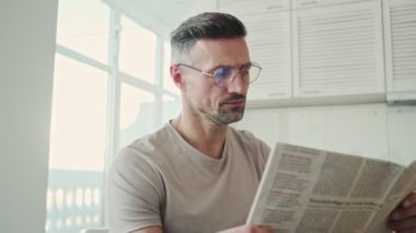 Ciddi bir adam sabahları mutfakta kahvaltı ederken gazete okuyor.