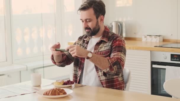 Evdeki Mutfaktaki Yakışıklı Neşeli Sakallı Adam Kahvaltısını Cep Telefonuyla Çekiyor — Stok video