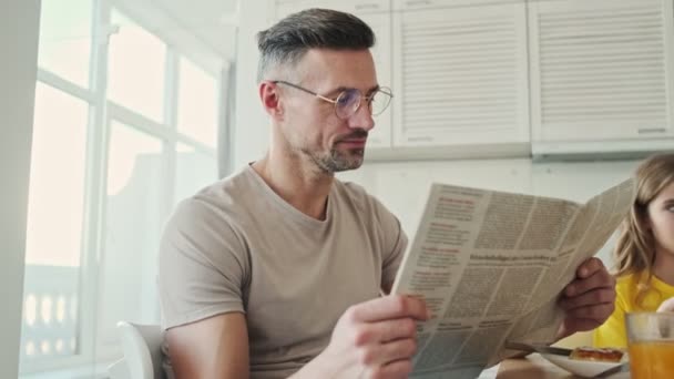 Ένας Όμορφος Άντρας Διαβάζει Εφημερίδα Ενώ Τρώει Πρωινό Στην Κουζίνα — Αρχείο Βίντεο