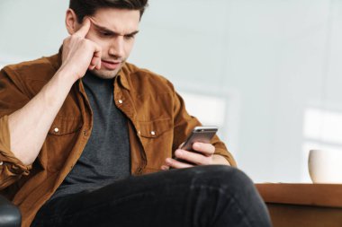 Ofiste çalışırken cep telefonu kullanan yakışıklı, kara kara düşünen beyaz adam.