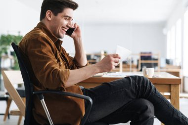 Ofiste belgelerle uğraşırken cep telefonuyla konuşan yakışıklı, gülümseyen bir genç resmi