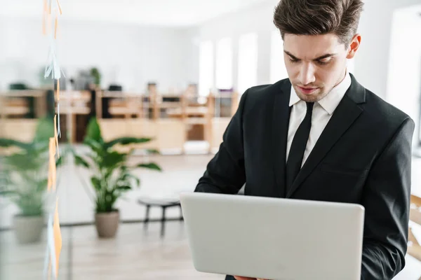 オフィスで働きながらノートパソコンを使ったスーツ姿の若いビジネスマンの集中イメージ — ストック写真