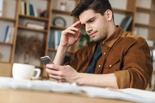 Imagen Joven Guapo Melancólico Usando Teléfono Celular Mientras Toma Café — Foto de Stock