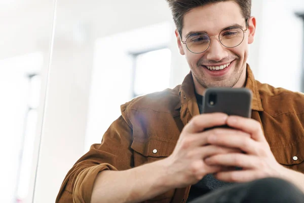 Imagem Belo Jovem Alegre Sorrindo Usando Celular Enquanto Trabalhava Escritório — Fotografia de Stock