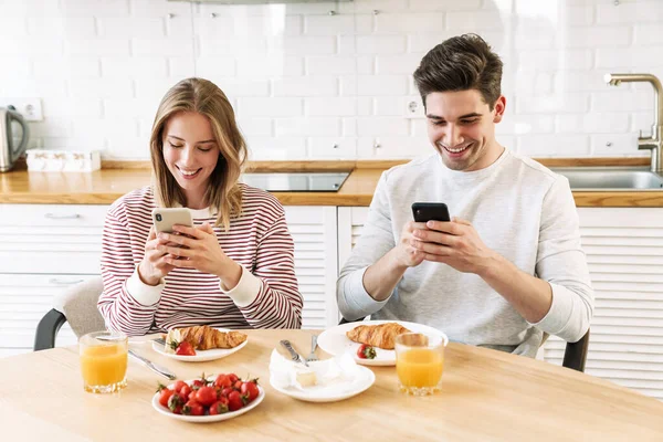 Retrato Una Joven Pareja Sonriente Usando Teléfonos Inteligentes Mientras Desayunaba — Foto de Stock