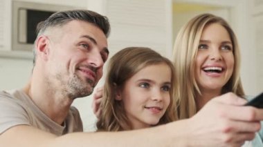 Gülümseyen genç bir aile evde televizyon izlerken patlamış mısır yiyor.