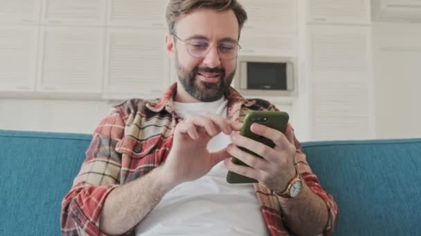 Schöner Junger Bärtiger Mann Sitzt Hause Auf Einem Sofa Und — Stockvideo