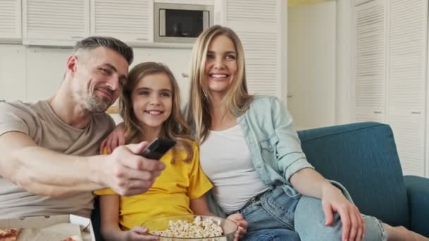 一个快乐快乐的微笑的年轻家庭一边在客厅里一起看电视一边吃爆米花 — 图库视频影像