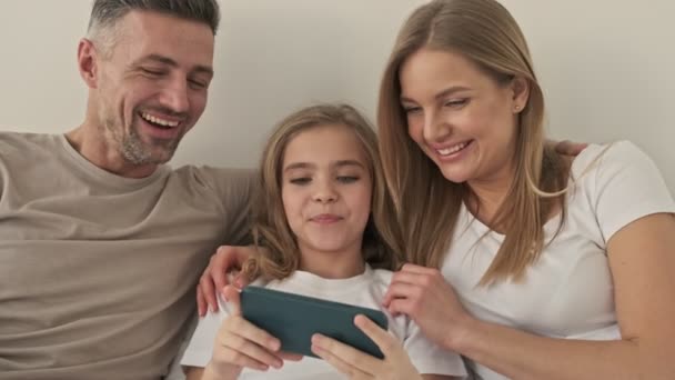一个快乐的家庭正在床上看着智能手机里有趣的东西 — 图库视频影像