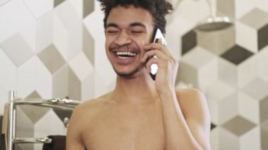 Genç iyimser gülen Afrikalı adam banyoda cep telefonuyla konuşuyor.
