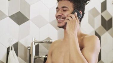 Genç mutlu Afrikalı adam banyoda cep telefonuyla konuşuyor.