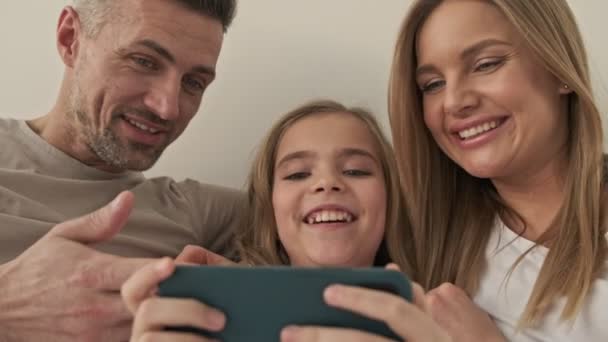 一个快乐家庭的特写正在床铺的智能手机上观看一些有趣的事情 — 图库视频影像