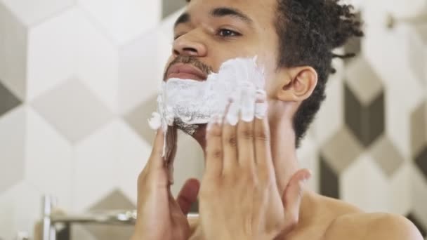 Jovem Africano Concentrado Usando Creme Barbear Perto Espelho Dentro Casa — Vídeo de Stock