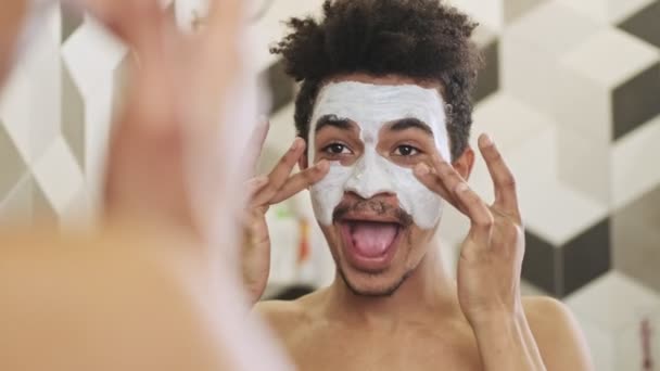 Νεαρός Χαρούμενος Αφρικανός Που Φροντίζει Δέρμα Του Μάσκα Προσώπου Κοντά — Αρχείο Βίντεο