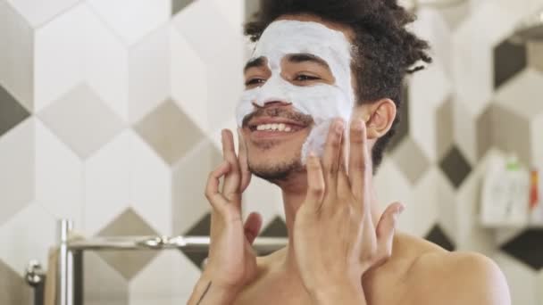 Νεαρός Χαρούμενος Αφρικανός Που Φροντίζει Δέρμα Του Μάσκα Προσώπου Κοντά — Αρχείο Βίντεο
