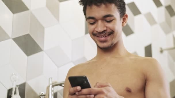 Joven Chico Africano Feliz Utilizando Teléfono Móvil Interior Baño — Vídeo de stock