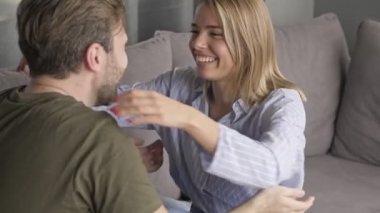 Evdeki oturma odasında otururken gülümseyen ve sarılan sevimli beyaz bir çift.