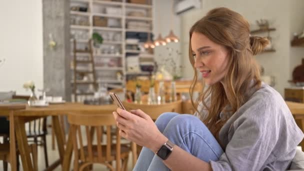 Een Mooie Jonge Vrouw Gebruikt Haar Smartphone Zittend Een Gezellige — Stockvideo