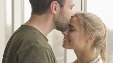Sevimli genç bir çift birbirlerine bakıyor ve evlerinin penceresinin yanında dikilirken sarılıyorlar.