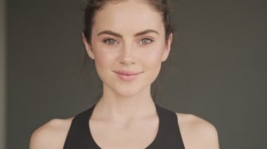 Gri bir stüdyoda genç ve mutlu bir kadının yakın çekimi kameraya gülümsüyor.