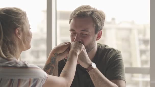 一个恋爱中的男人正在亲吻他坐在家里的年轻漂亮的女朋友的手 — 图库视频影像