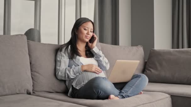 Una Bonita Embarazada Asiática Está Usando Portátil Hablando Teléfono Sentado — Vídeo de stock