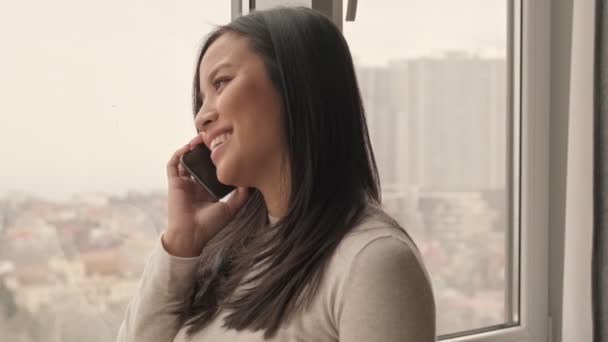 居間の自宅で電話で話していると にこやかな妊婦のアジア人女性が腹を撫でている — ストック動画