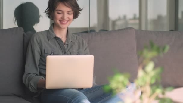 陽気若いですかわいいです女性使用してノートパソコン上のソファに座って自宅 — ストック動画